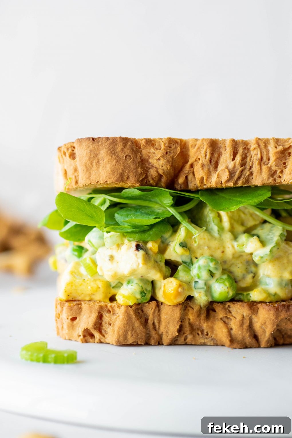 Close up side view of a chicken curry salad sandwich with bright greens on a white background.