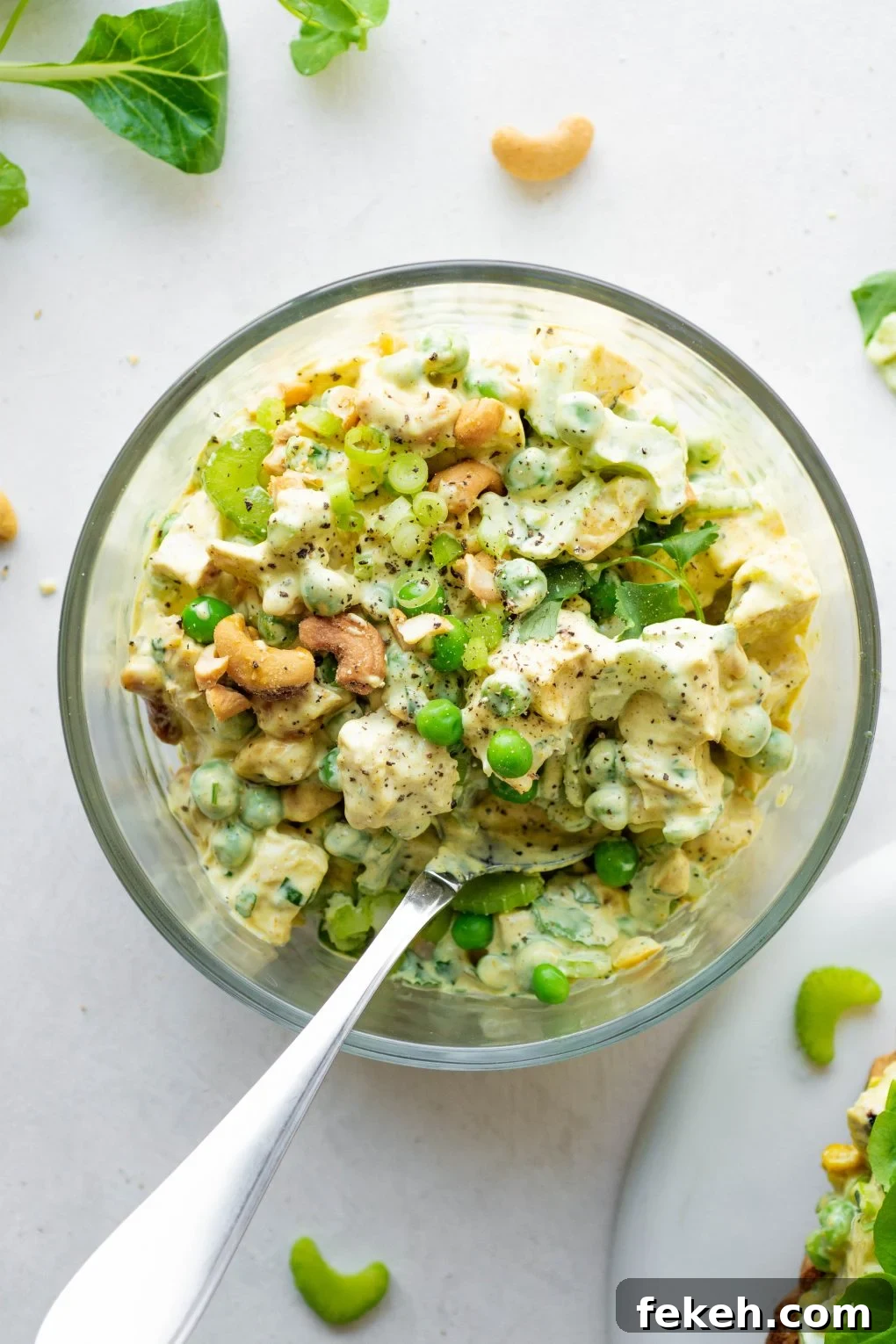 Overhead shot of a bowl of curried chicken salad with a spoon on a white background