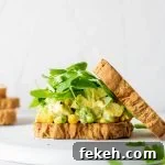 Side view of a curried chicken salad sandwich with some fresh greens and the top piece of bread angled off to the side. On a white background.