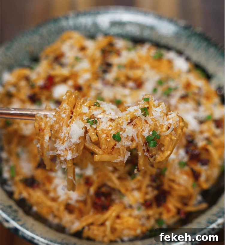 Close-up of a forkful of chili oil caramelized onion pasta topped with parmesan and scallions.
