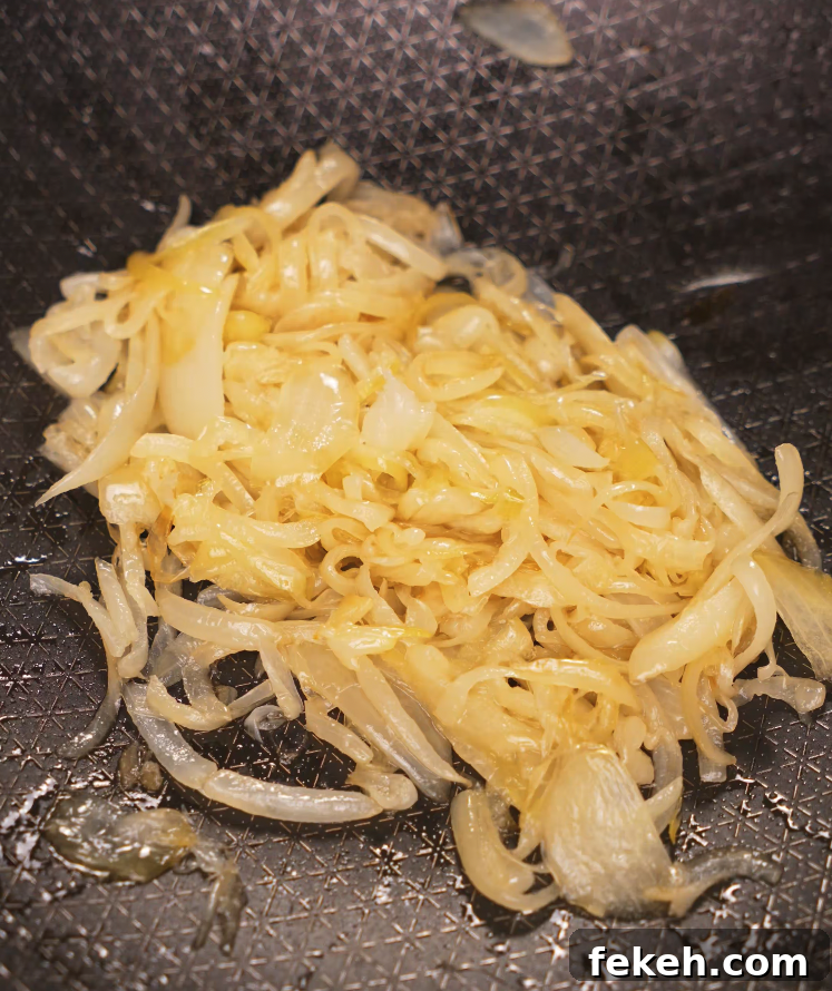 Thinly sliced onions caramelizing in oil in a nonstick pan for the base of the chili oil pasta.
