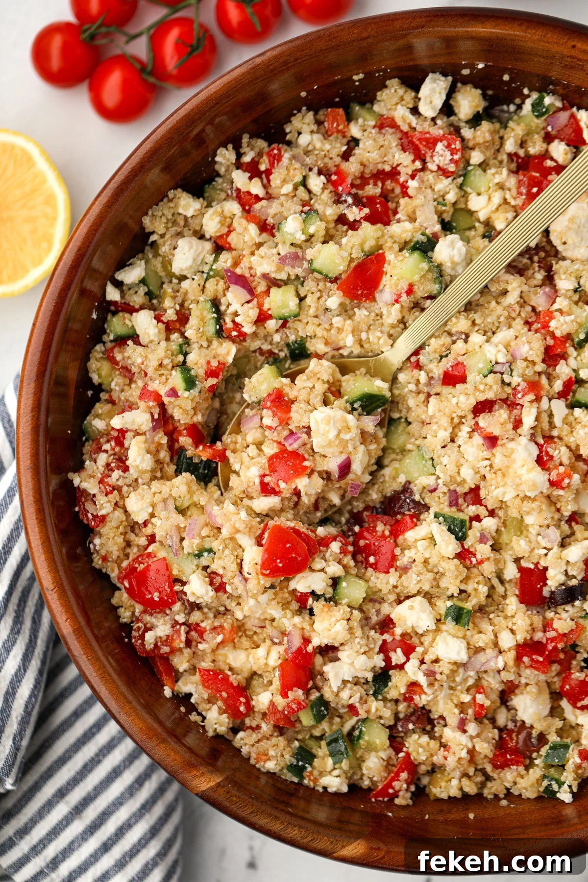 A large salad bowl filled with quinoa salad; pieces of red pepper, feta, and cucumber are visible.