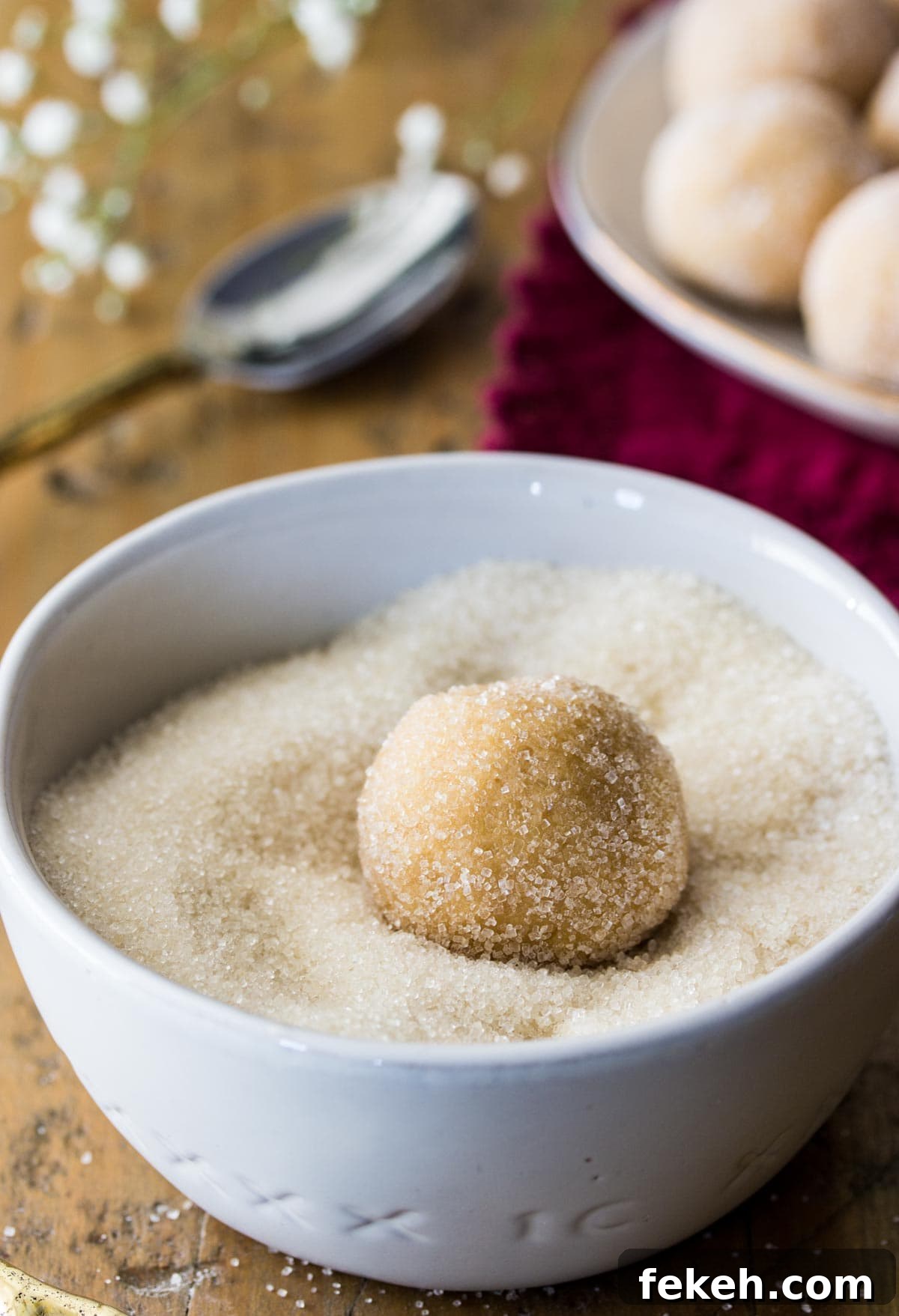 Peanut butter cookie dough ball being rolled through sugar.