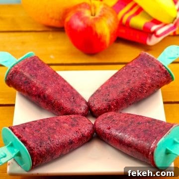 4 fruit popsicles on a white plate with fruit in background