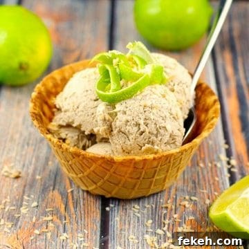banana nice cream in a waffle cone bowl with a spoon, garnished with coconut and lime zest , with whole limes in the background