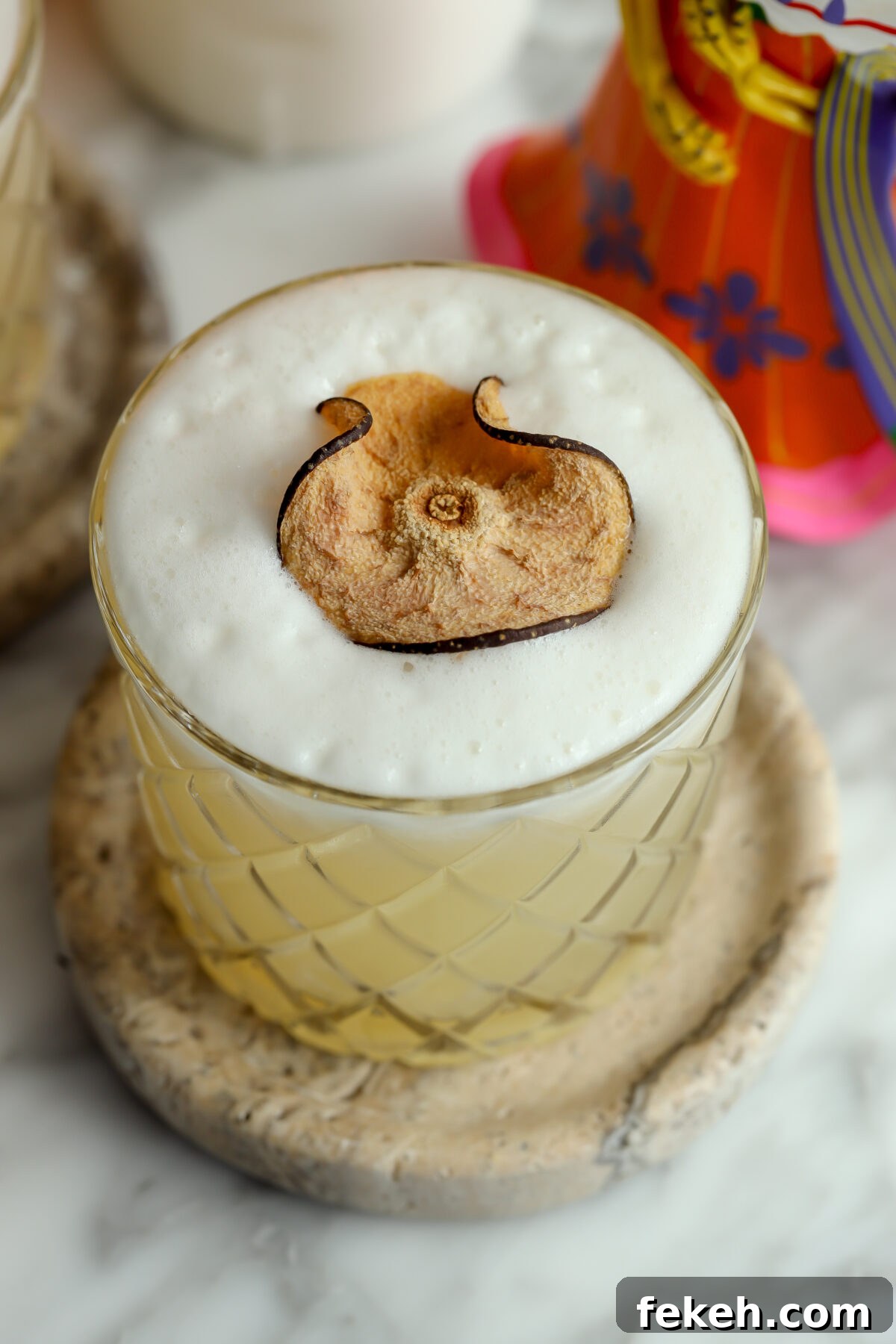 A beautiful cocktail with a foam top, garnished with a dried pear.
