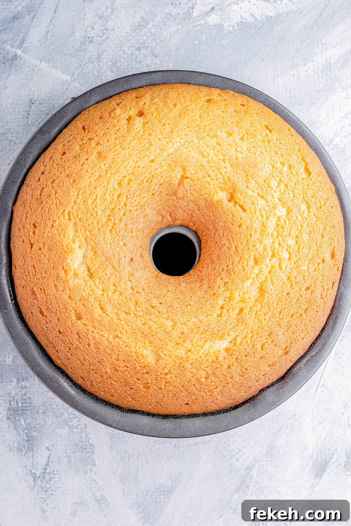Classic Cream Cheese Pound Cake Recipe for Moist, Tender Slices 12 A freshly baked round sponge cake in a bundt pan on a textured gray surface.