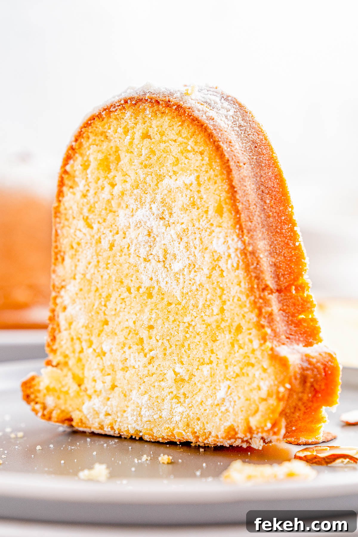 Classic Cream Cheese Pound Cake Recipe for Moist, Tender Slices 15 A slice of bundt cake dusted with powdered sugar on a gray plate.