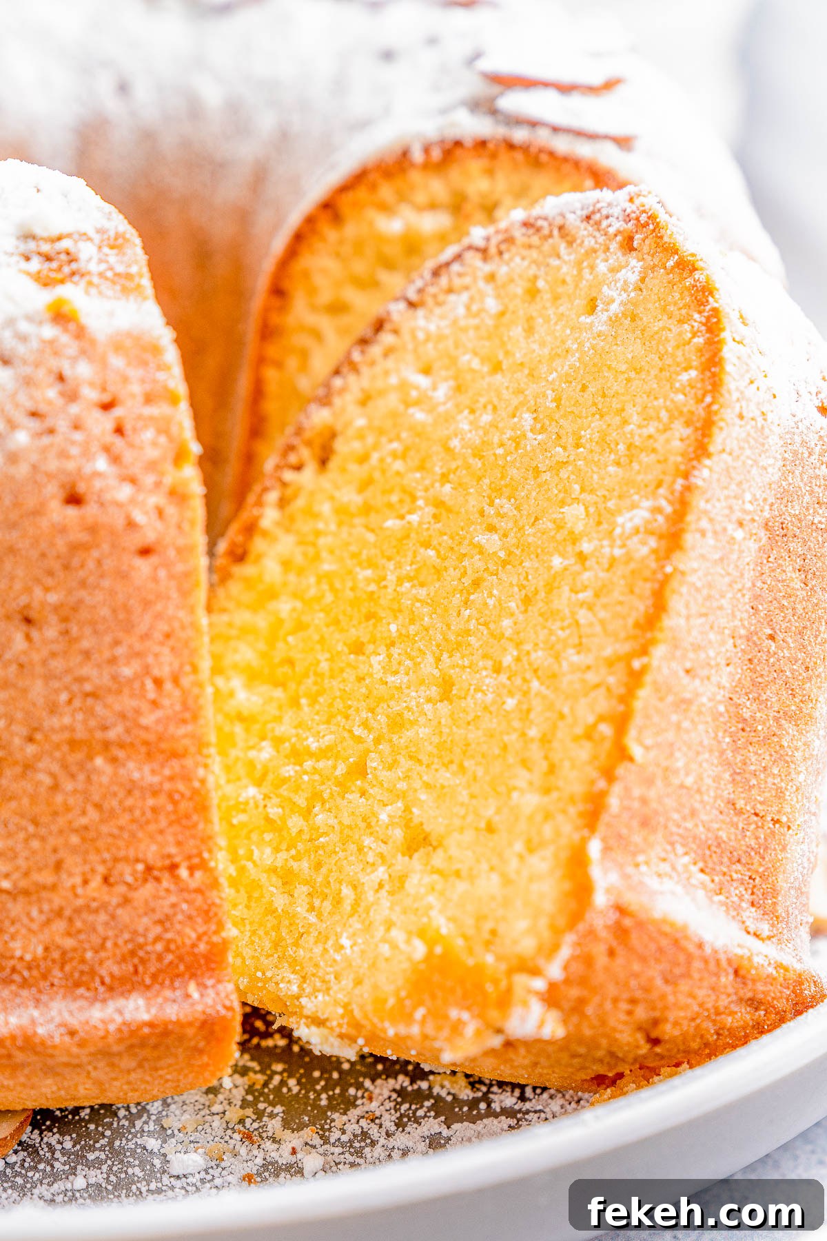 Classic Cream Cheese Pound Cake Recipe for Moist, Tender Slices 3 A close-up of a sliced bundt cake dusted with powdered sugar on a white plate.