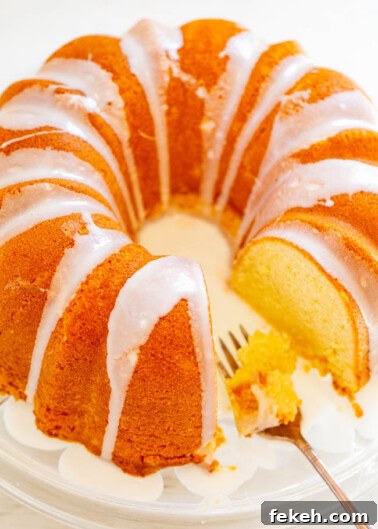 Classic Cream Cheese Pound Cake Recipe for Moist, Tender Slices 23 A sliced bundt cake with white glaze on a glass serving plate with a fork.