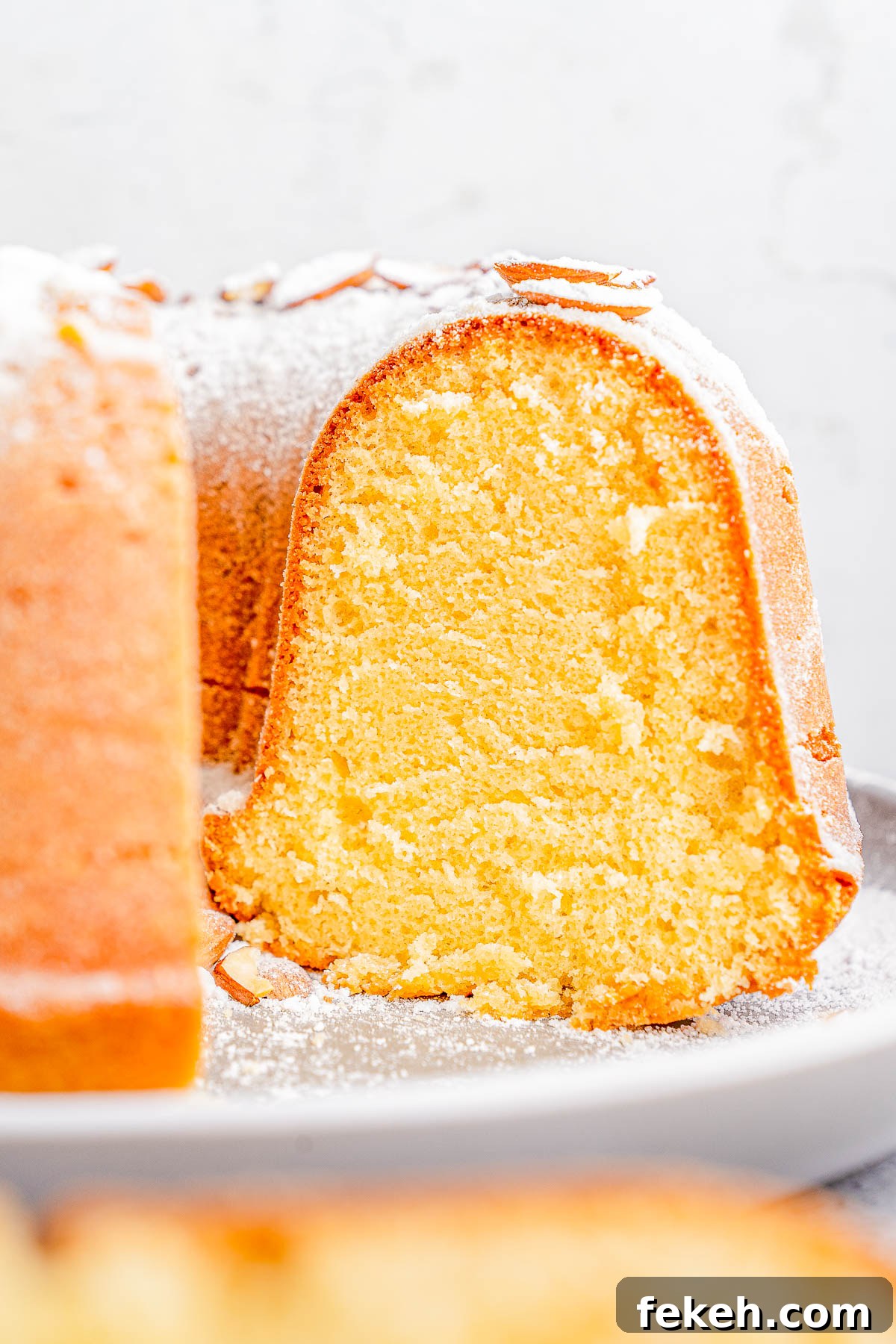 Classic Cream Cheese Pound Cake Recipe for Moist, Tender Slices 4 A close-up of a sliced Bundt cake dusted with powdered sugar on a plate.