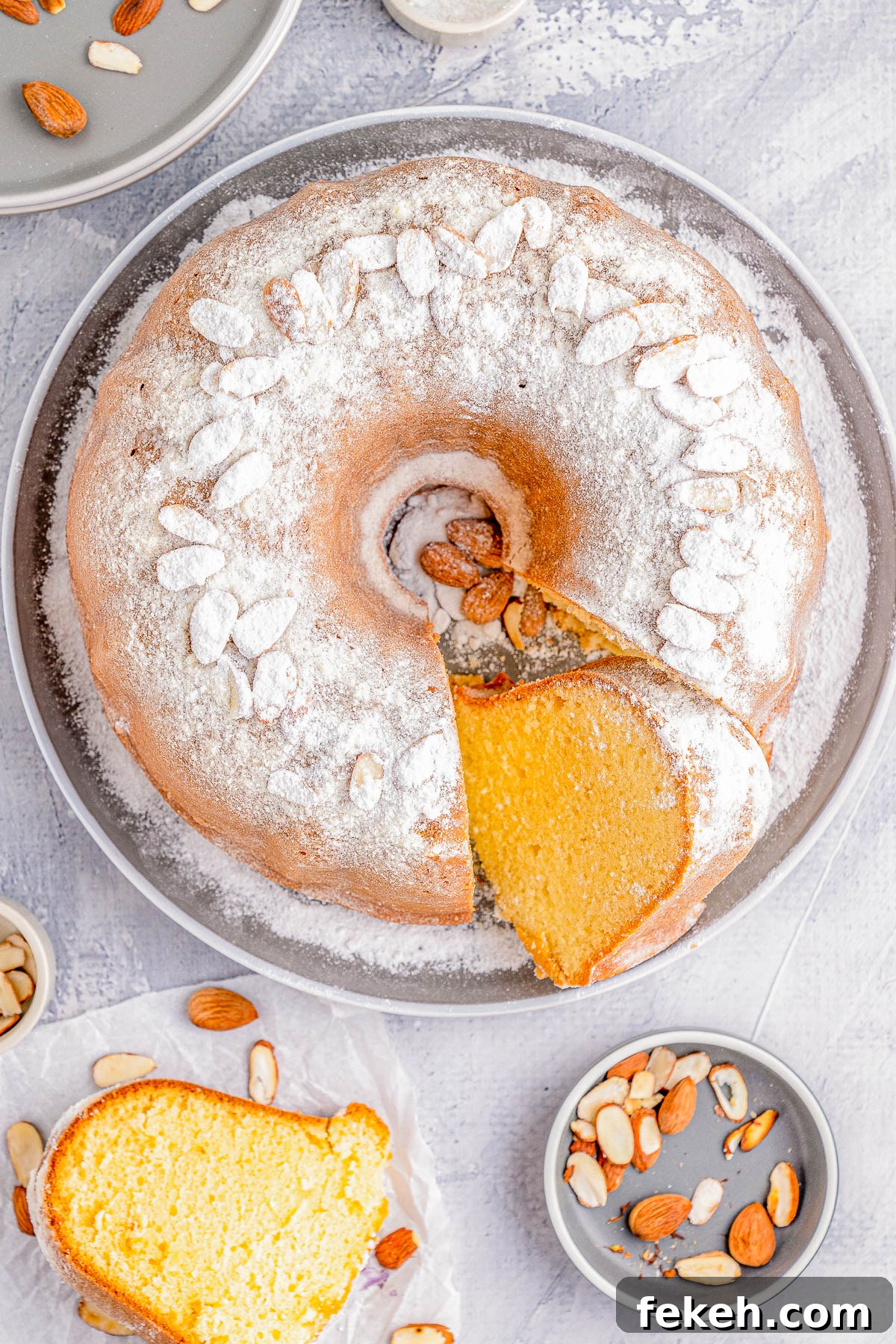 Classic Cream Cheese Pound Cake Recipe for Moist, Tender Slices 6 A bundt cake dusted with powdered sugar and topped with almonds. A slice is cut and placed on a plate. Additional almonds are scattered around.