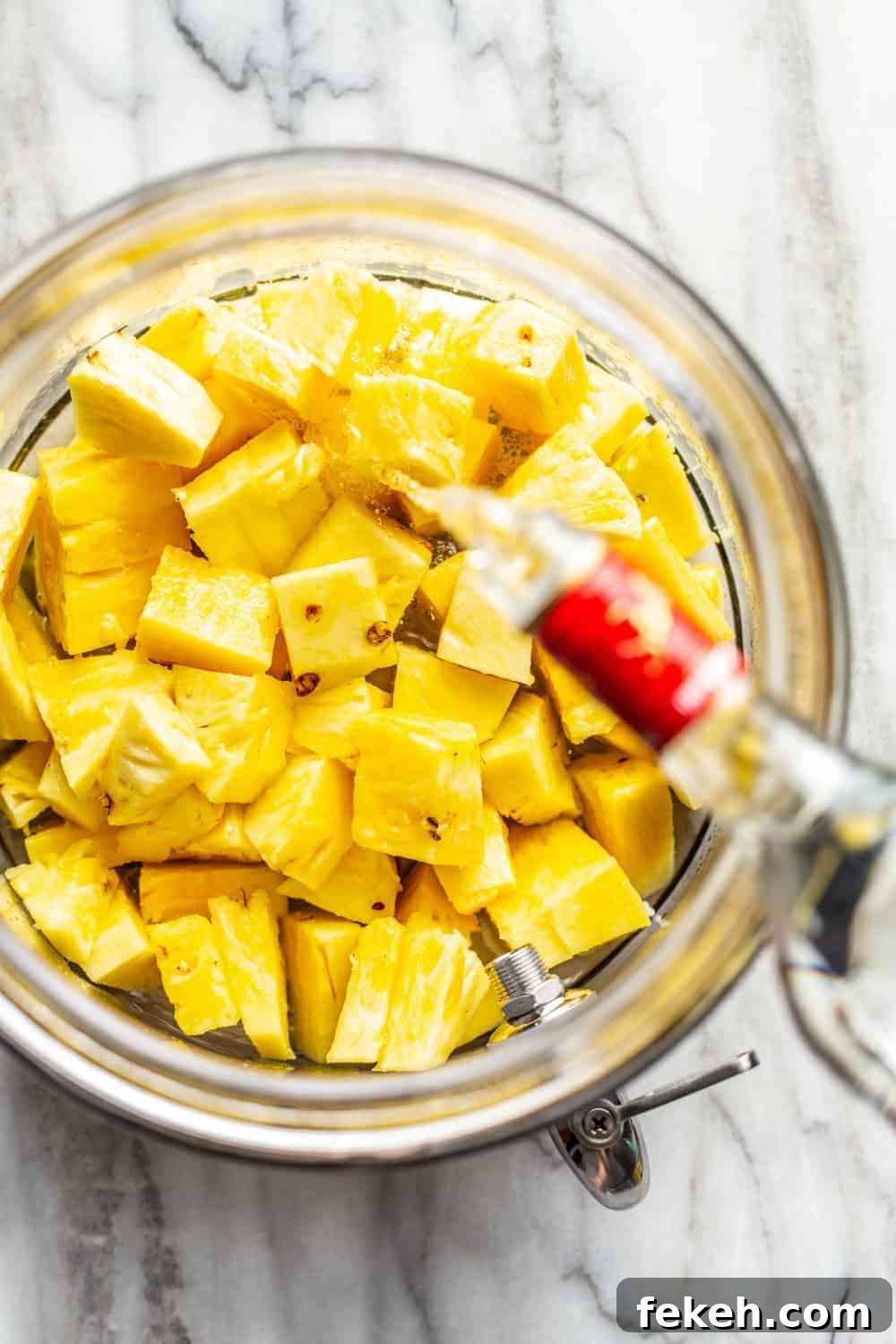 How to Make Stoli Doli: Puerto Rican Coconut Rum Dessert Recipe 6 Vodka being poured over diced pineapple in a glass container