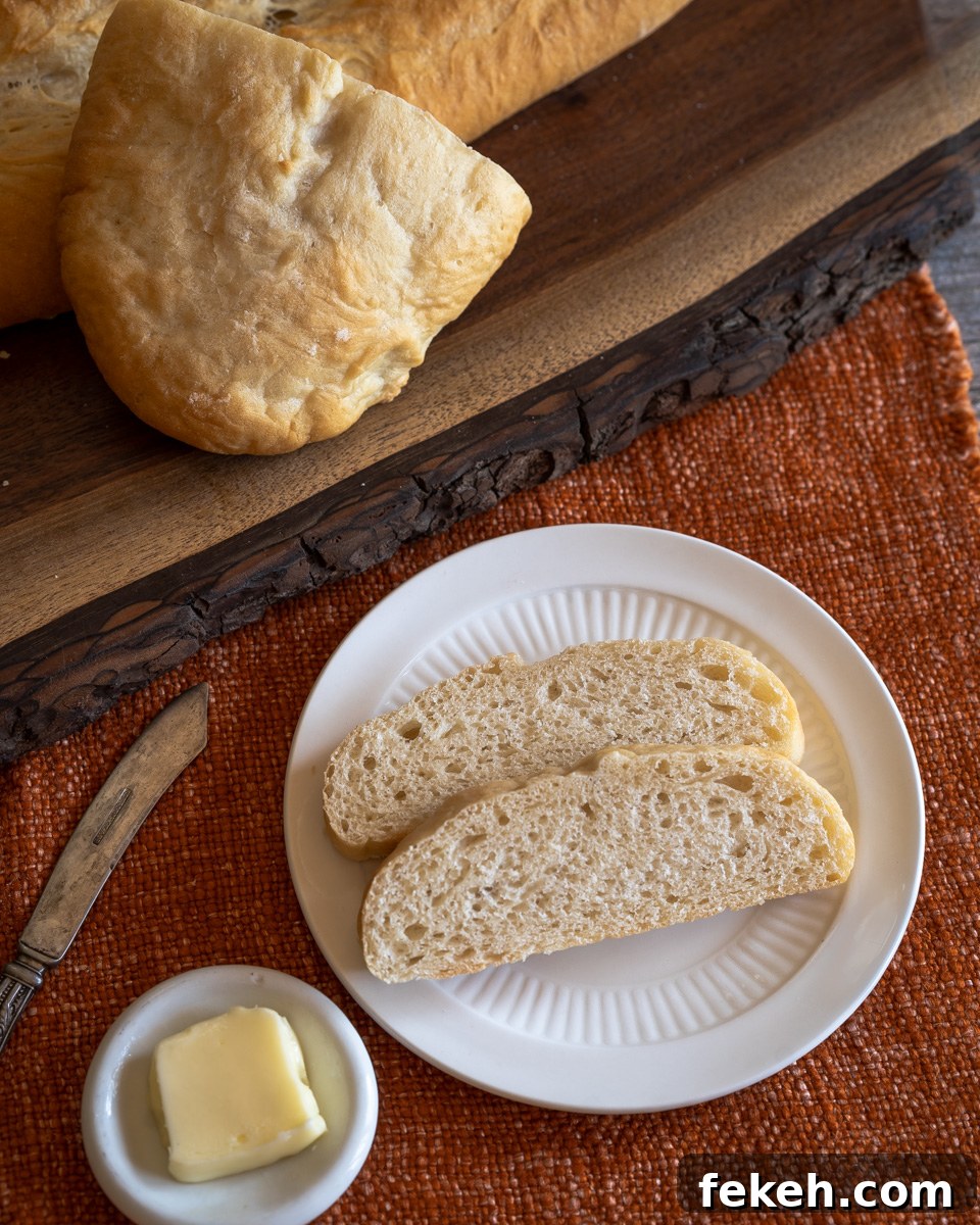 Authentic Cuban Bread (Pan Cubano) Recipe for Crispy Loaf 12 Top-down view of two slices of Pan Cubano bread with the loaf in the background. - Hostess At Heart