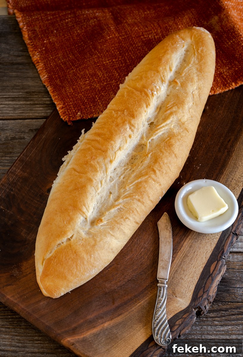 Authentic Cuban Bread (Pan Cubano) Recipe for Crispy Loaf 3 A bread baguette sitting on a cutting board next to a dish holding butter - Hostess At Heart