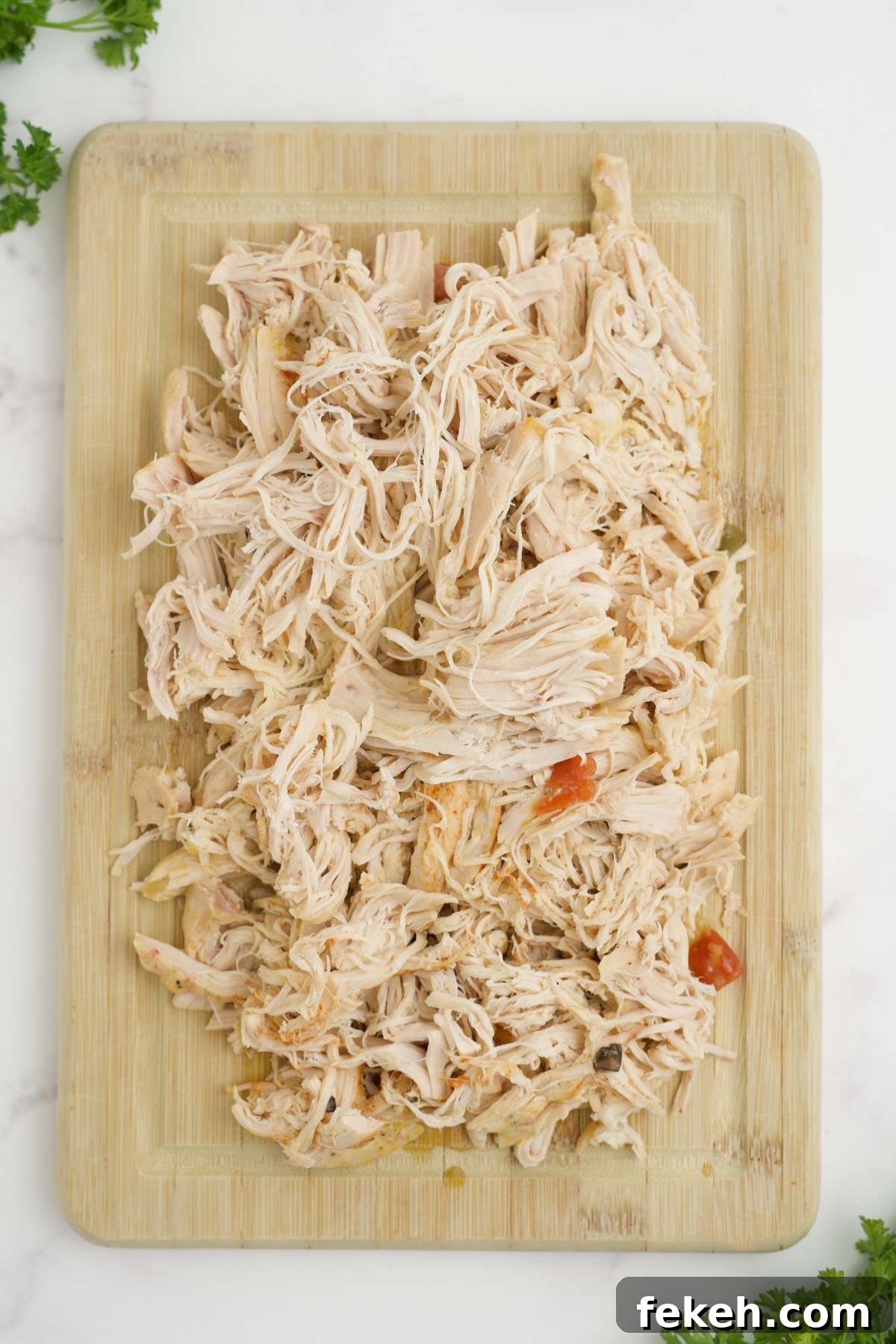Chicken shredded on wooden cutting board.