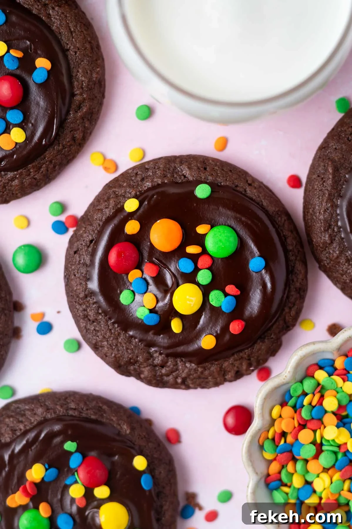 Fudgy Cosmic Brownie Cookie Recipe for Gooey Chocolate Lovers 3 cosmic brownie cookies with ganache and colored candy topping and a glass of milk and bowl of sprinkles