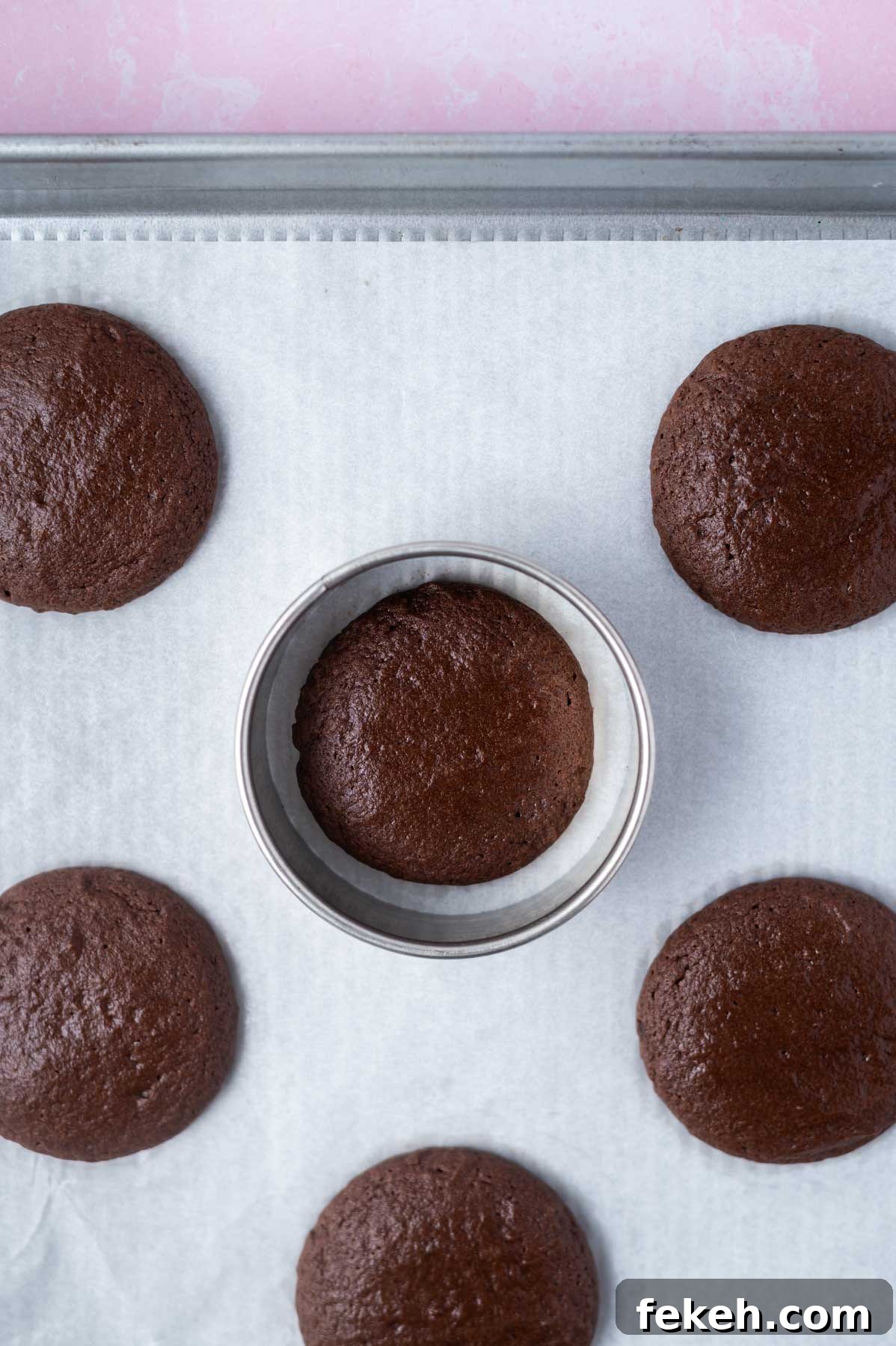 Fudgy Cosmic Brownie Cookie Recipe for Gooey Chocolate Lovers 10 baked brownie cookies on a a baking pan with a biscuit cutter "scooting" a cookie