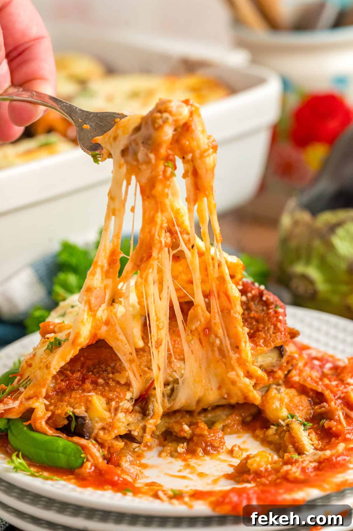 A fork pulling up the cheese on a slice of eggplant parmesan A fork pulling up the cheese on a slice of eggplant parmesan