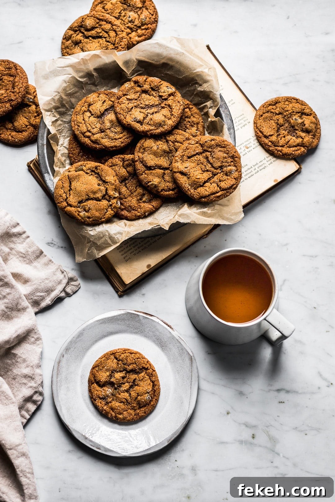 Table scene of ginger molasses cookies in container with book, plate and tea nearby