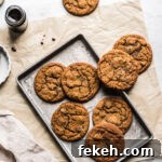 Ginger cookies on a baking sheet resting on a brown parchment paper rectangle. A jar of molasses is nearby.
