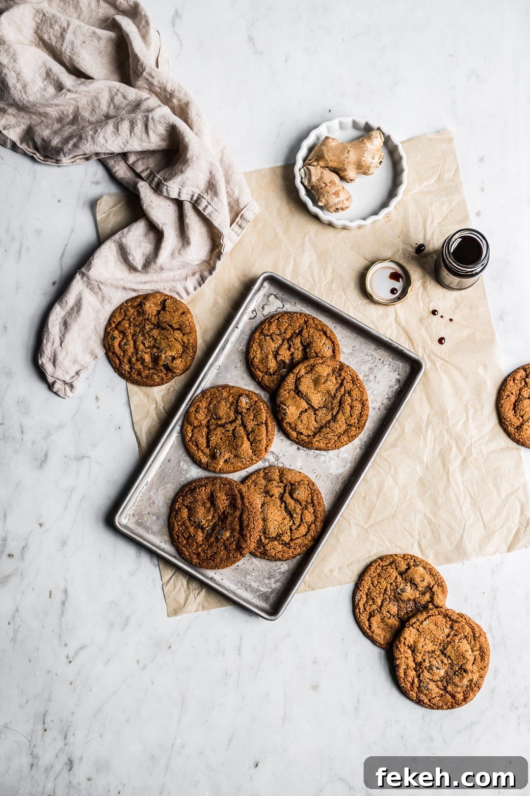 Cookies on pan with ginger and molasses nearby - all on a white marble background