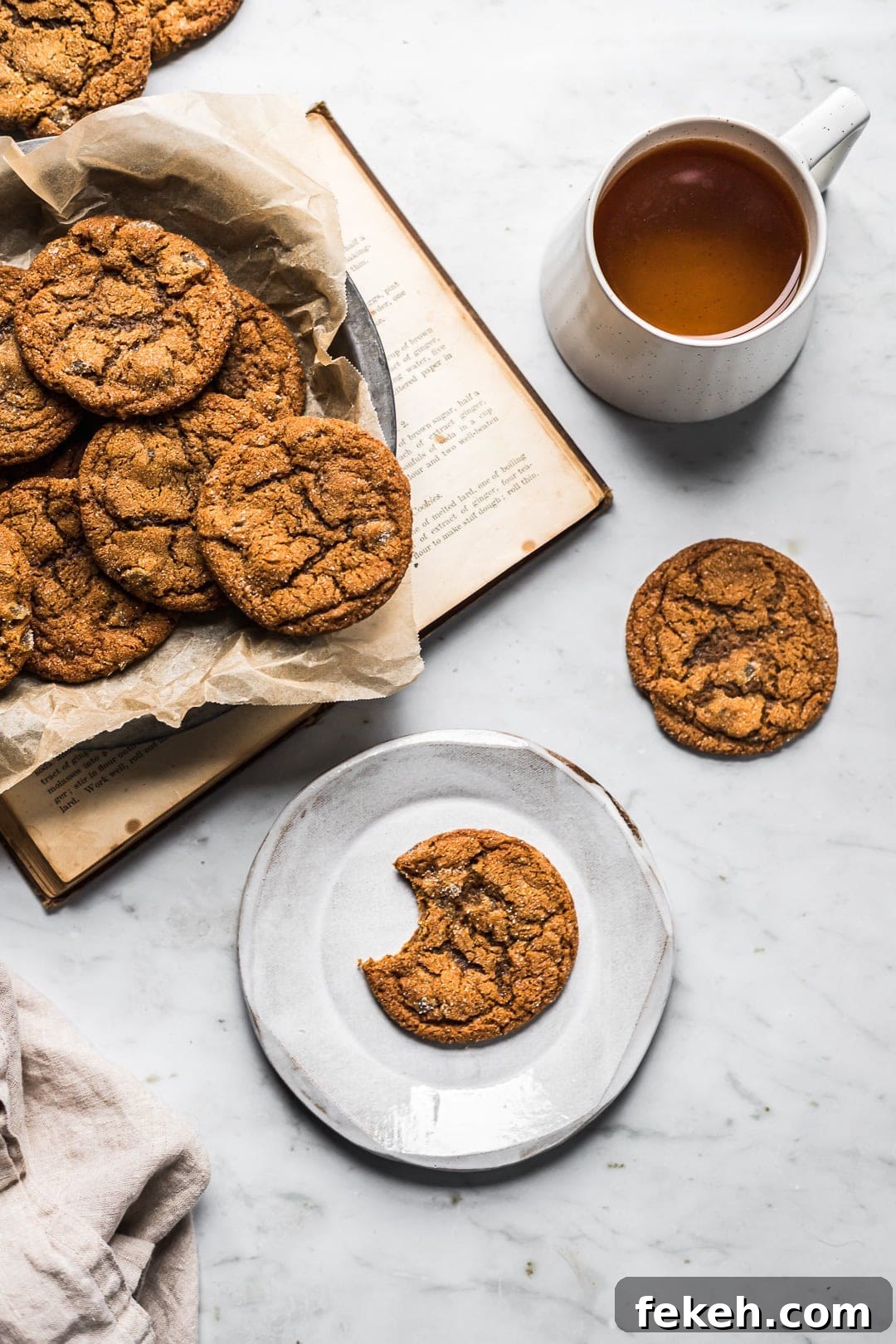 Cookies on a dish with book, tea and plate nearby on a marble surface
