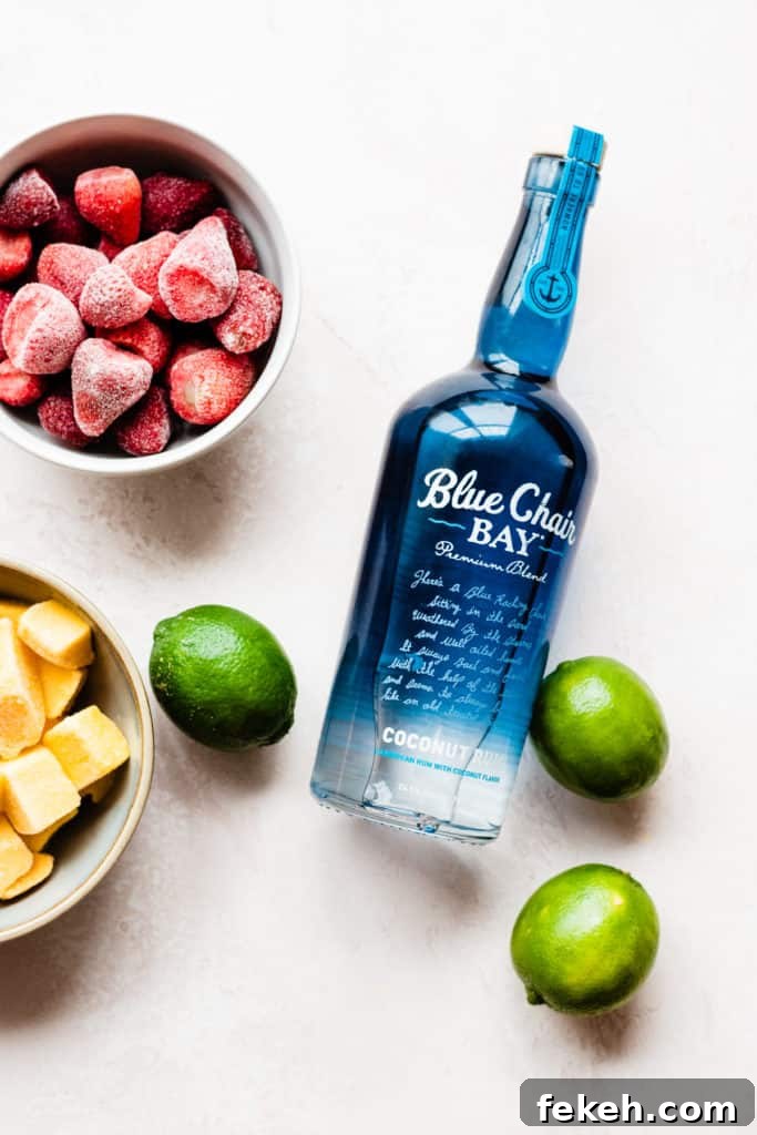 A bowl of frozen strawberries, frozen mango, and a few limes scattered around a blue Blue Chair Bay Rum Coconut Rum bottle