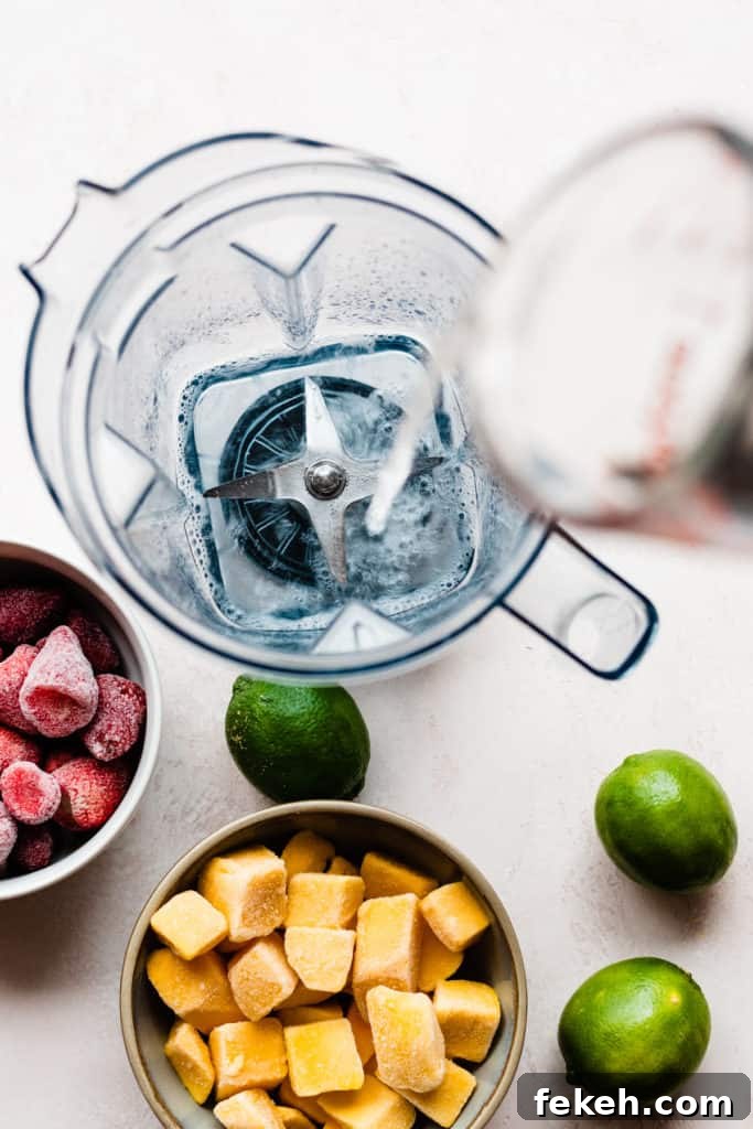 Coconut rum being poured into a blender, with strawberries, mango, and limes scattered around
