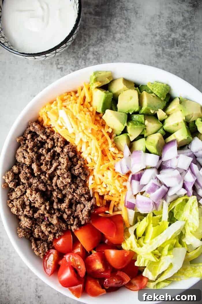 Low-Carb Keto Taco Salad Recipe for Quick Weeknight Meals 2 large white bowl containing keto taco salad next to a small bowl containing sour cream