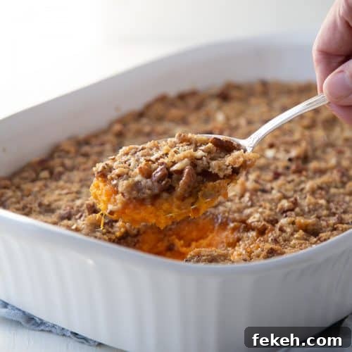 hand with a spoon of sweet potato casserole, lifting it out of a white casserole dish.