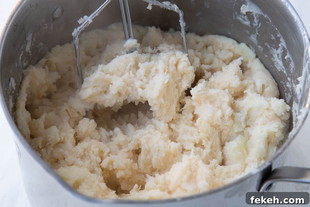 potato masher mashing potatoes in a large pot.
