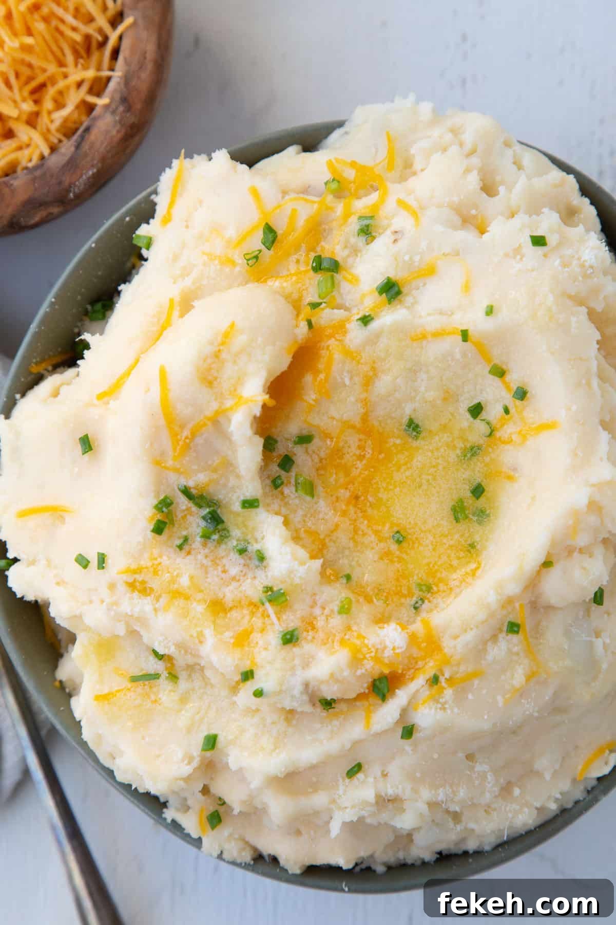 cheesy mashed potatoes in a green bowl, topped with chives and melted butter.