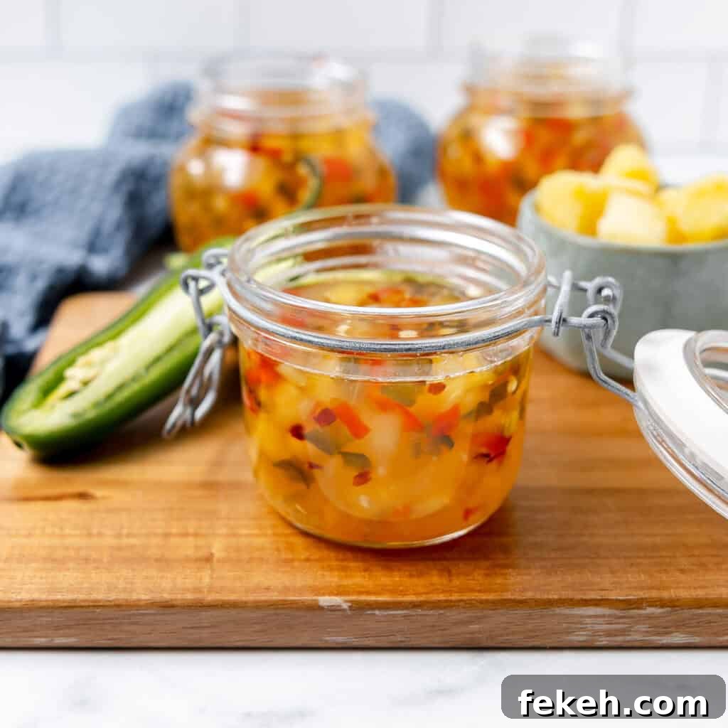 Pineapple Jalapeño Jam Recipe: Sweet-Spicy Preserves Guide 2 An open glass jar of pineapple relish with diced peppers sits on a wooden board, next to a jalapeño and additional jars in the background.