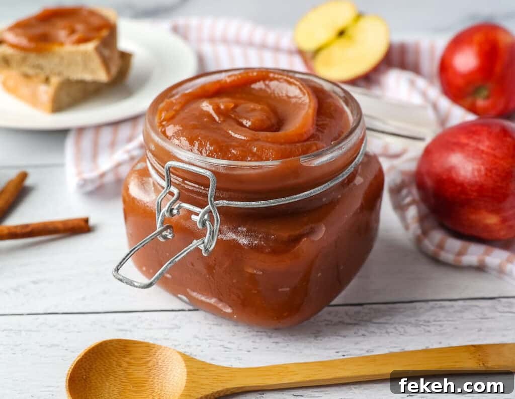 Pineapple Jalapeño Jam Recipe: Sweet-Spicy Preserves Guide 13 A jar of apple butter with a wooden spoon in the front, apples in the background.