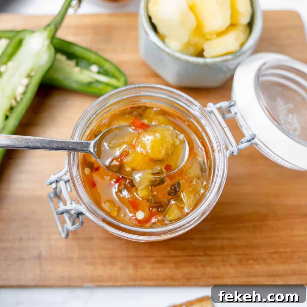 Pineapple Jalapeño Jam Recipe: Sweet-Spicy Preserves Guide 3 A spoonful of pineapple jalapeño jelly being lifted from a glass jar; sliced jalapeños and pineapple chunks are on a wooden surface nearby.