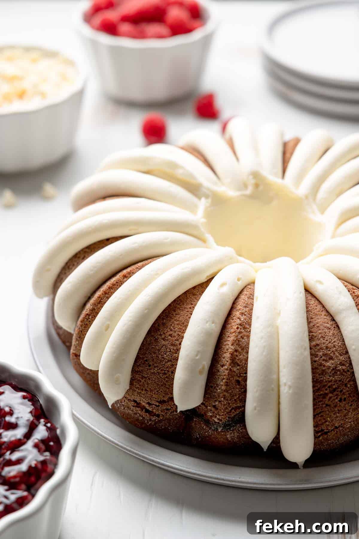 Bundt cake with cream cheese icing piped around the cake next to raspberries and white chocolate chips.
