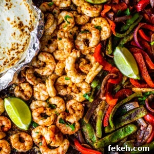 Sheet Pan Shrimp Fajitas with Peppers and Lime 9 Sheet pan covered with peppers, onions and shrimp with some lime wedges and soft shell tortillas on the side.