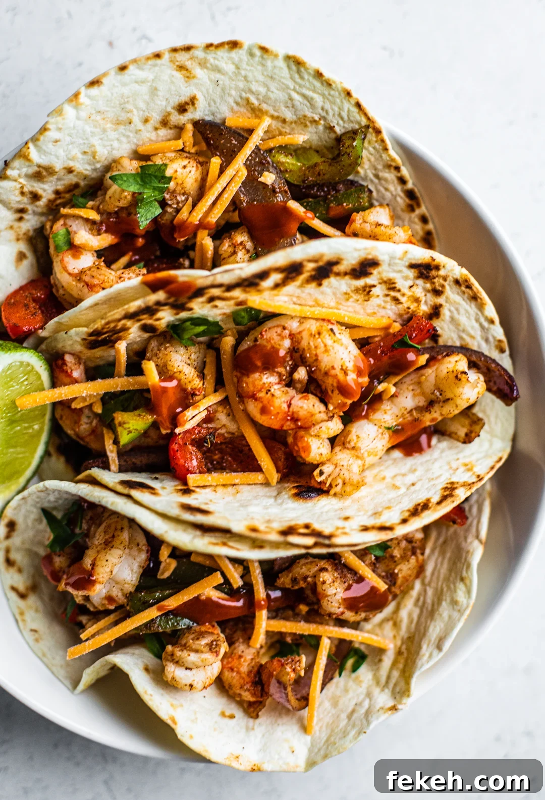 Sheet Pan Shrimp Fajitas with Peppers and Lime 8 Overhead shot of shrimp fajitas folded in a bowl with a lime wedge.