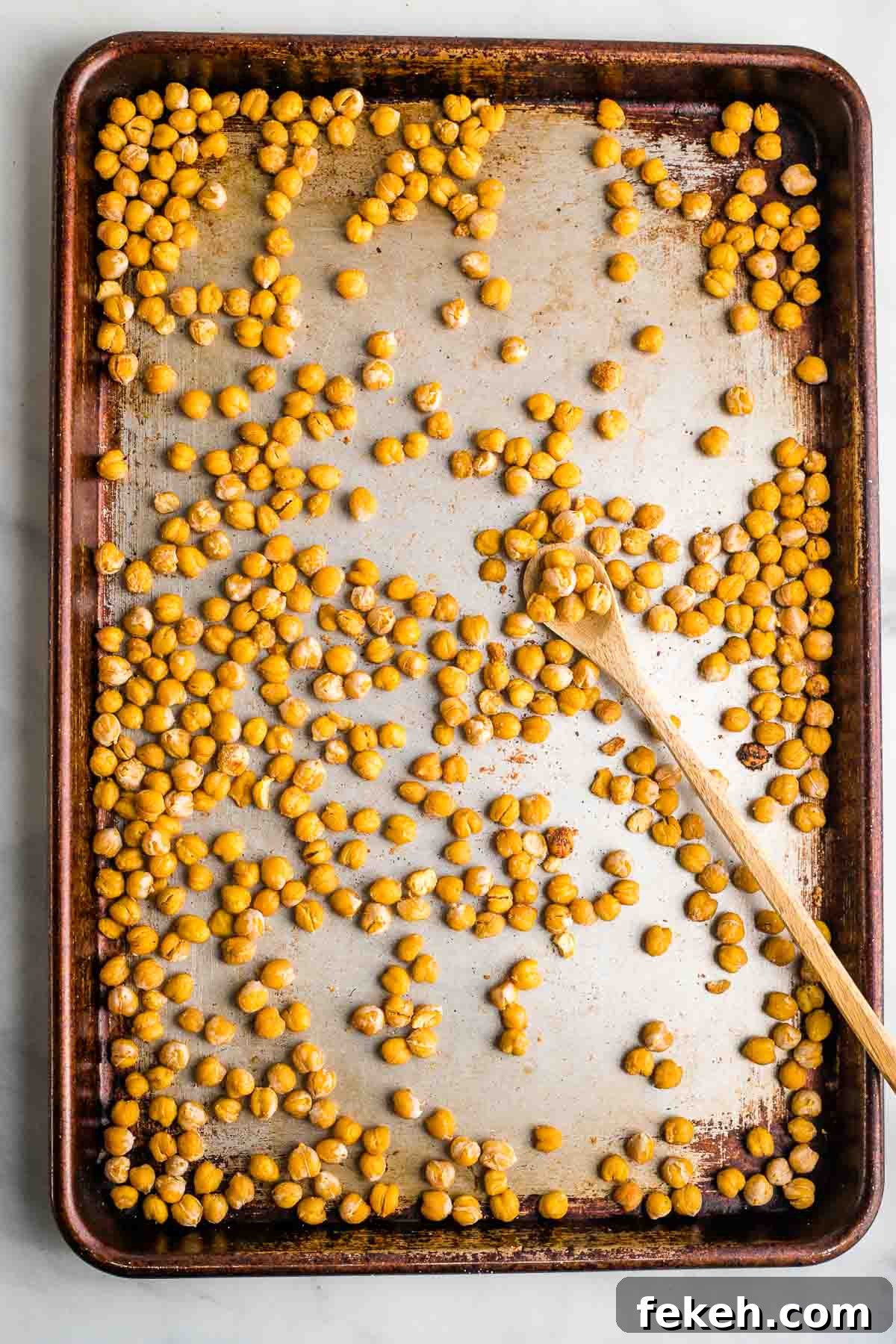 Crunchy roasted chickpeas on a baking sheet with spoon.