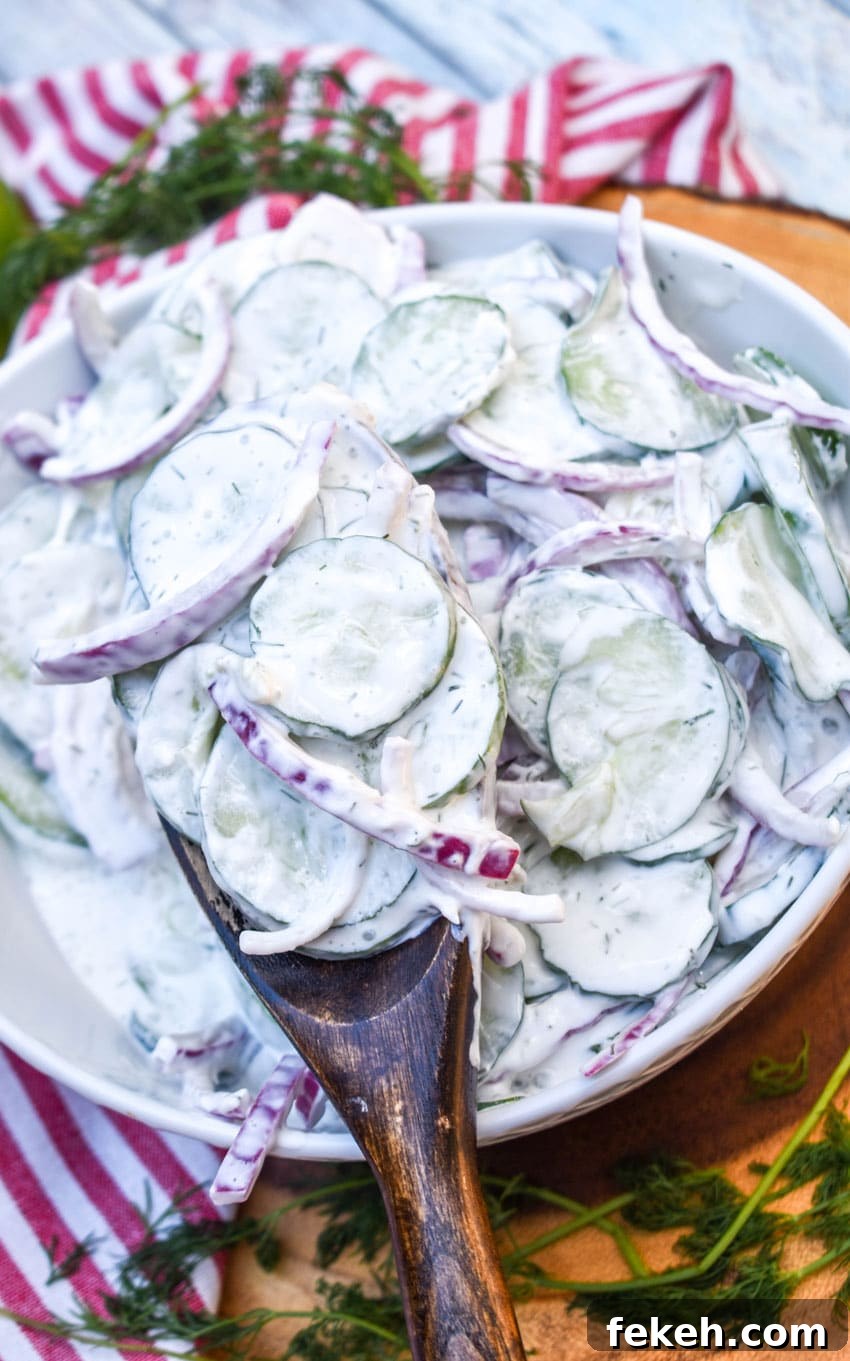 Creamy Cucumber Salad Recipe with Dill and Sour Cream 4 a wooden spoon scooping creamy cucumber salad out of a white serving bowl