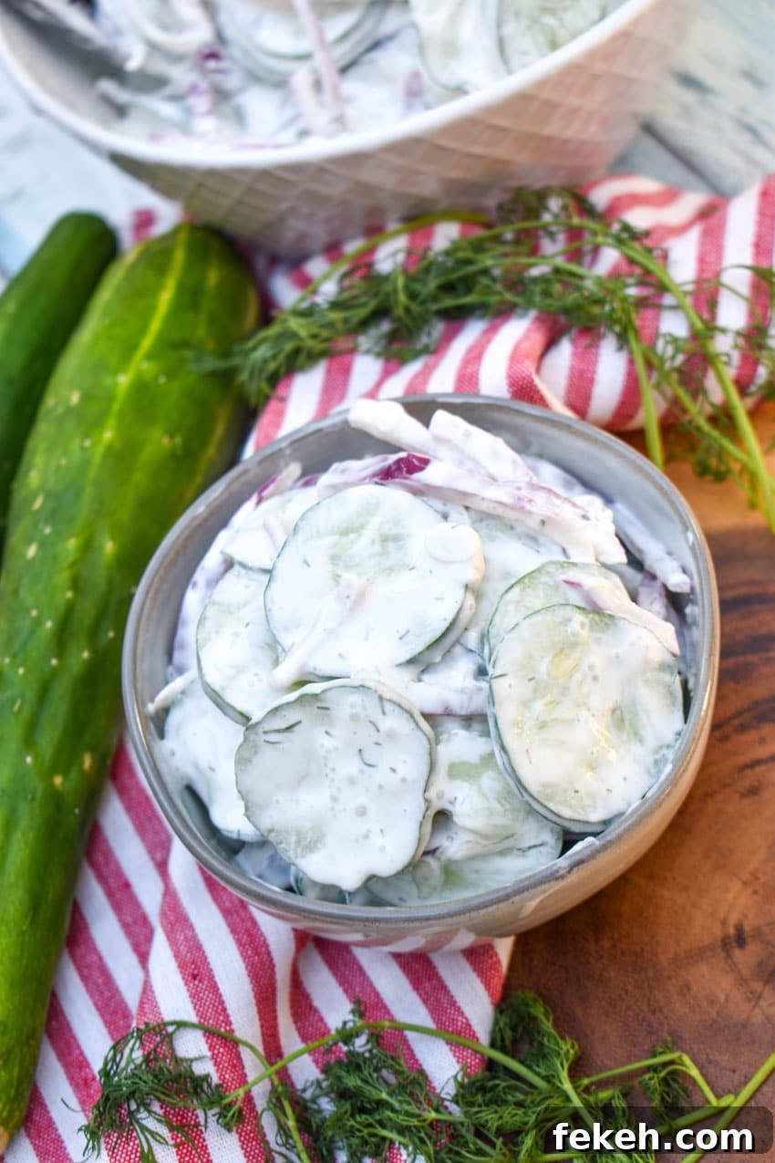 Creamy Cucumber Salad Recipe with Dill and Sour Cream 7 creamy cucumber salad in a small gray bowl on a wooden cutting board