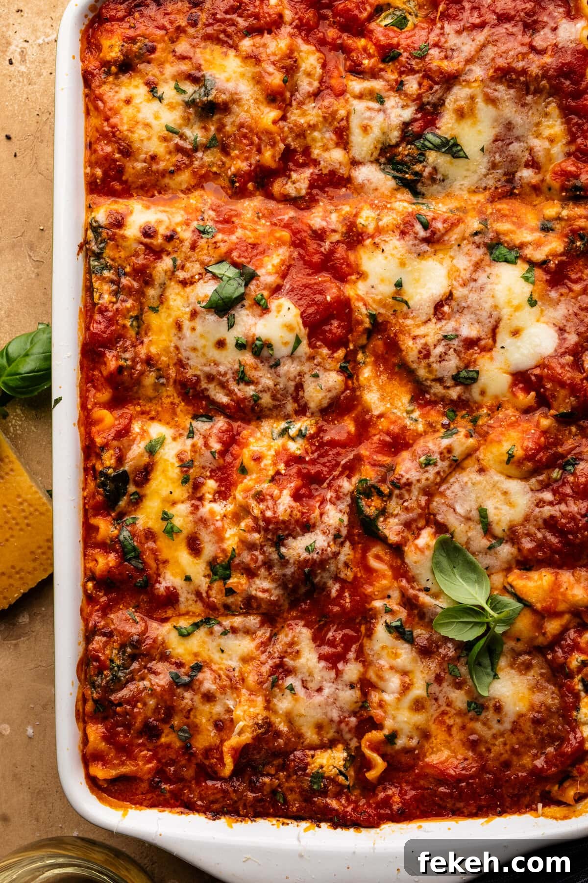 Creamy Spinach Lasagna Recipe with Ricotta and Mozzarella 7 A close-up of lasagna in a white dish. The lasagna has green herbs sprinkled over it and the dish is sitting on a tan background.