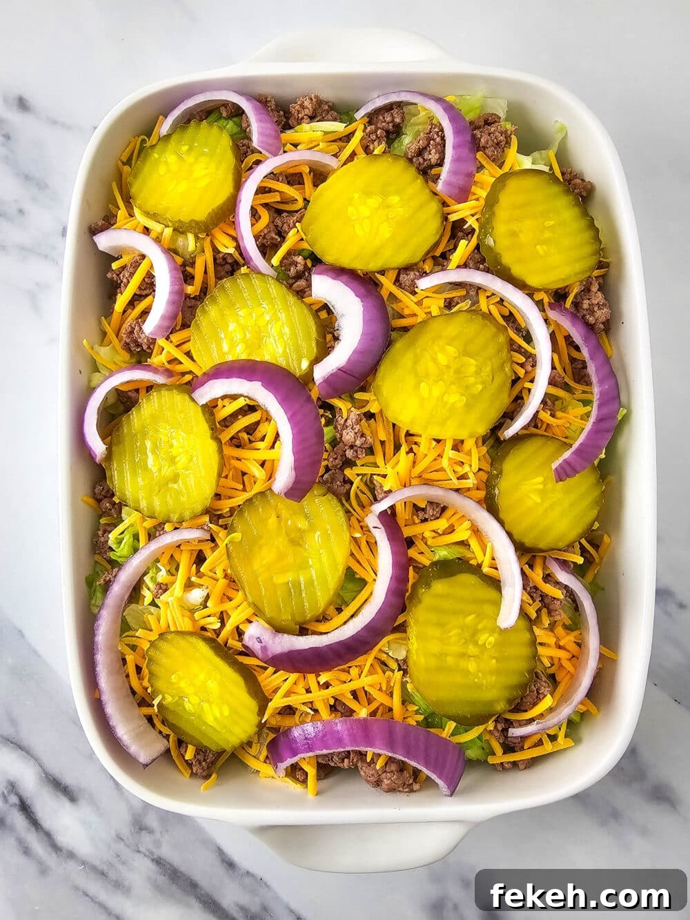 Keto Big Mac Salad: High-Protein Low-Carb Cheeseburger Bowl 12 chopped lettuce and ground beef and shredded cheese and pickles and onions in a casserole dish
