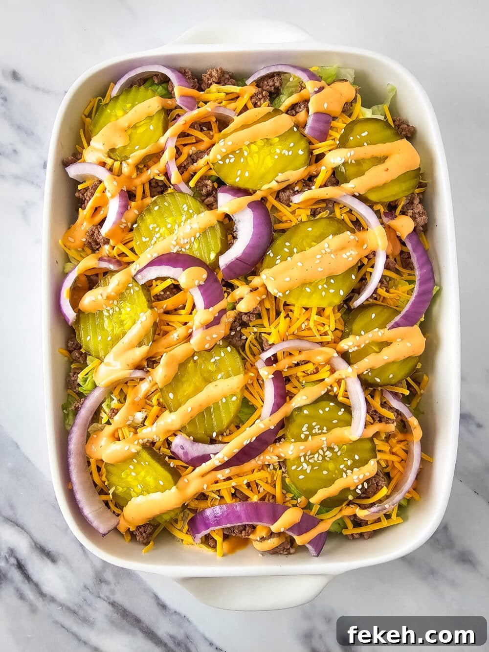 Keto Big Mac Salad: High-Protein Low-Carb Cheeseburger Bowl 14 chopped lettuce and ground beef and shredded cheese and pickles and onions and thousand island dressing and sesame seeds in a casserole dish