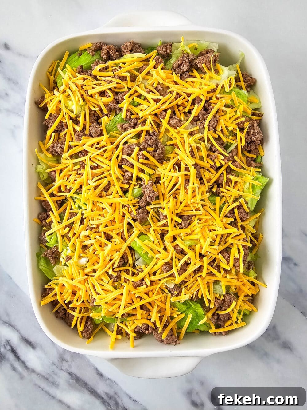 Keto Big Mac Salad: High-Protein Low-Carb Cheeseburger Bowl 10 chopped lettuce and ground beef and shredded cheese in a casserole dish
