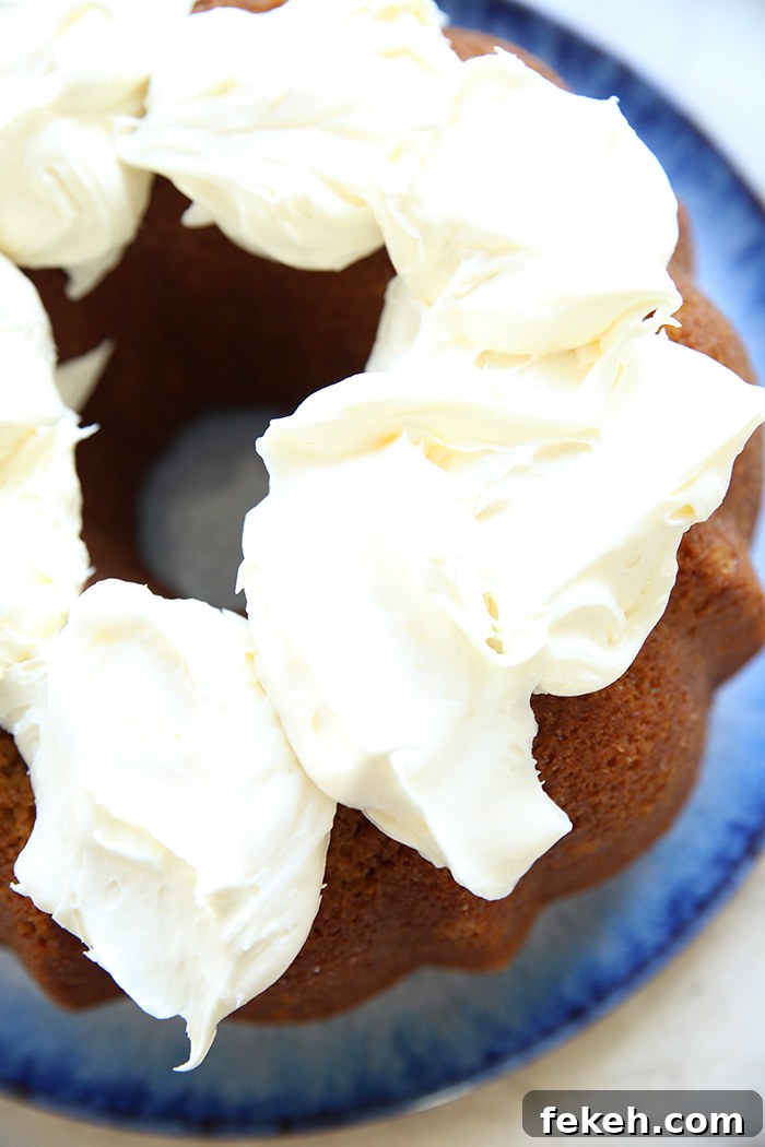A pumpkin bundt cake topped with dollops of cream cheese closely together sitting on a large round plate.