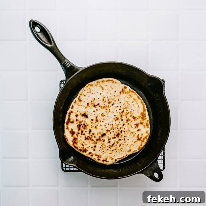 Authentic Greek Pita Bread Recipe: Soft, Foldable Pitas 8 Greek pita bread cooking in a hot cast iron pan with golden spots forming.