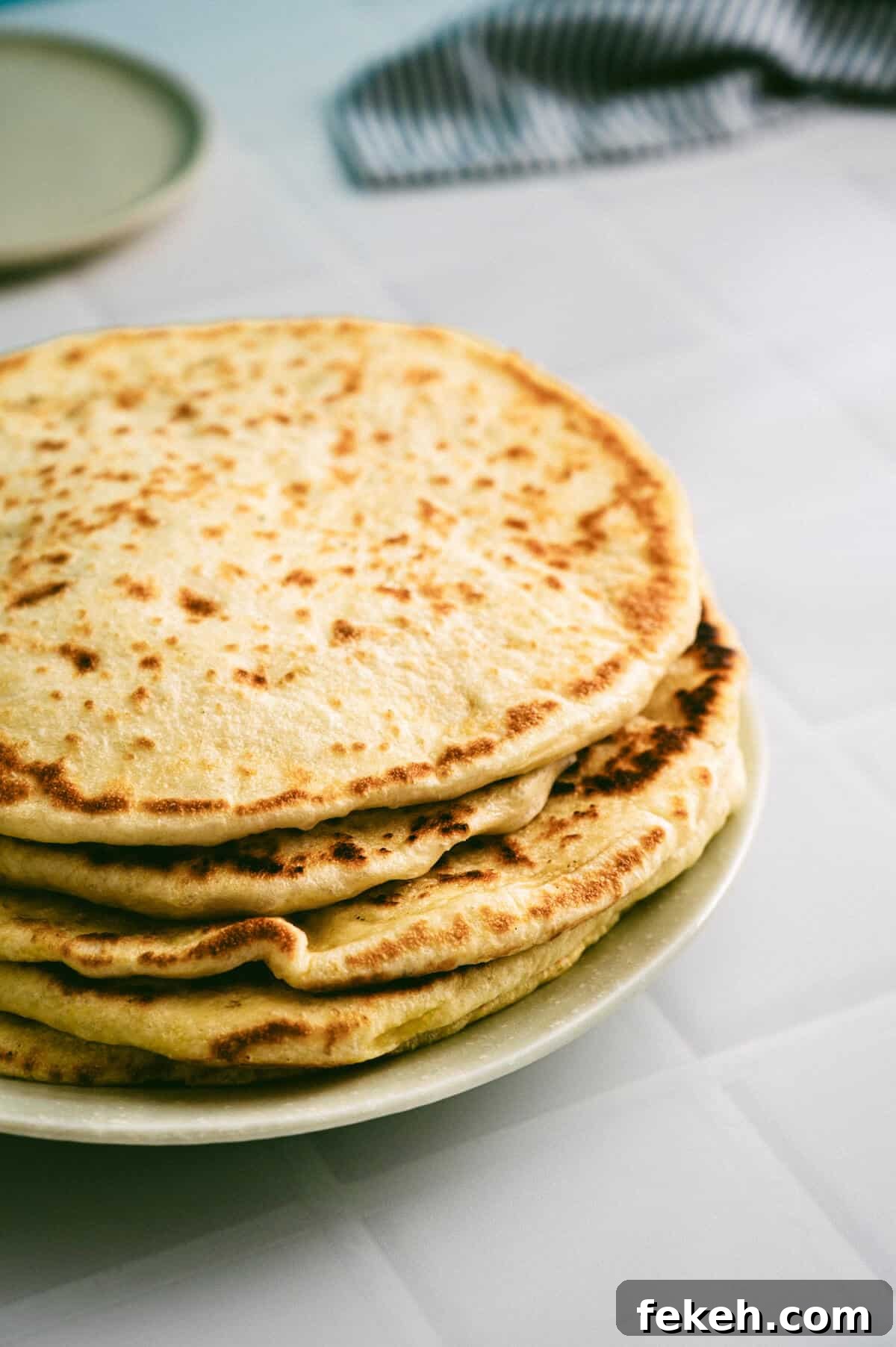 Authentic Greek Pita Bread Recipe: Soft, Foldable Pitas 10 Soft Greek pita bread stacked on a plate, lightly golden with charred spots.