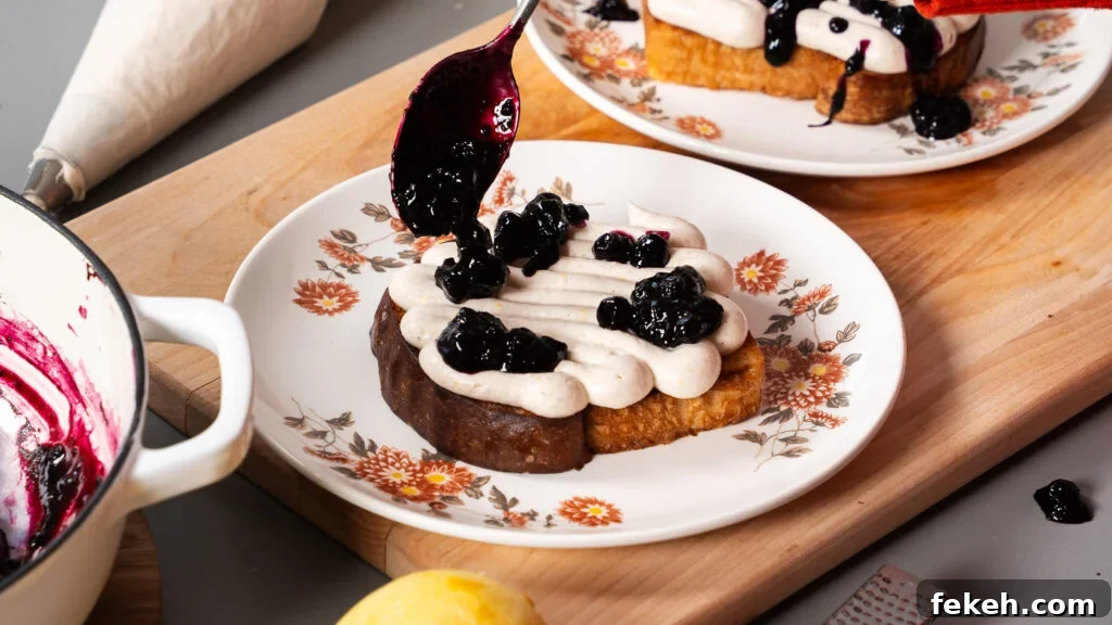 Lemon Ricotta Toast with Fresh Blueberries and Honey 3 Spooning blueberries on top of a whipped ricotta cheese mixture on toast.